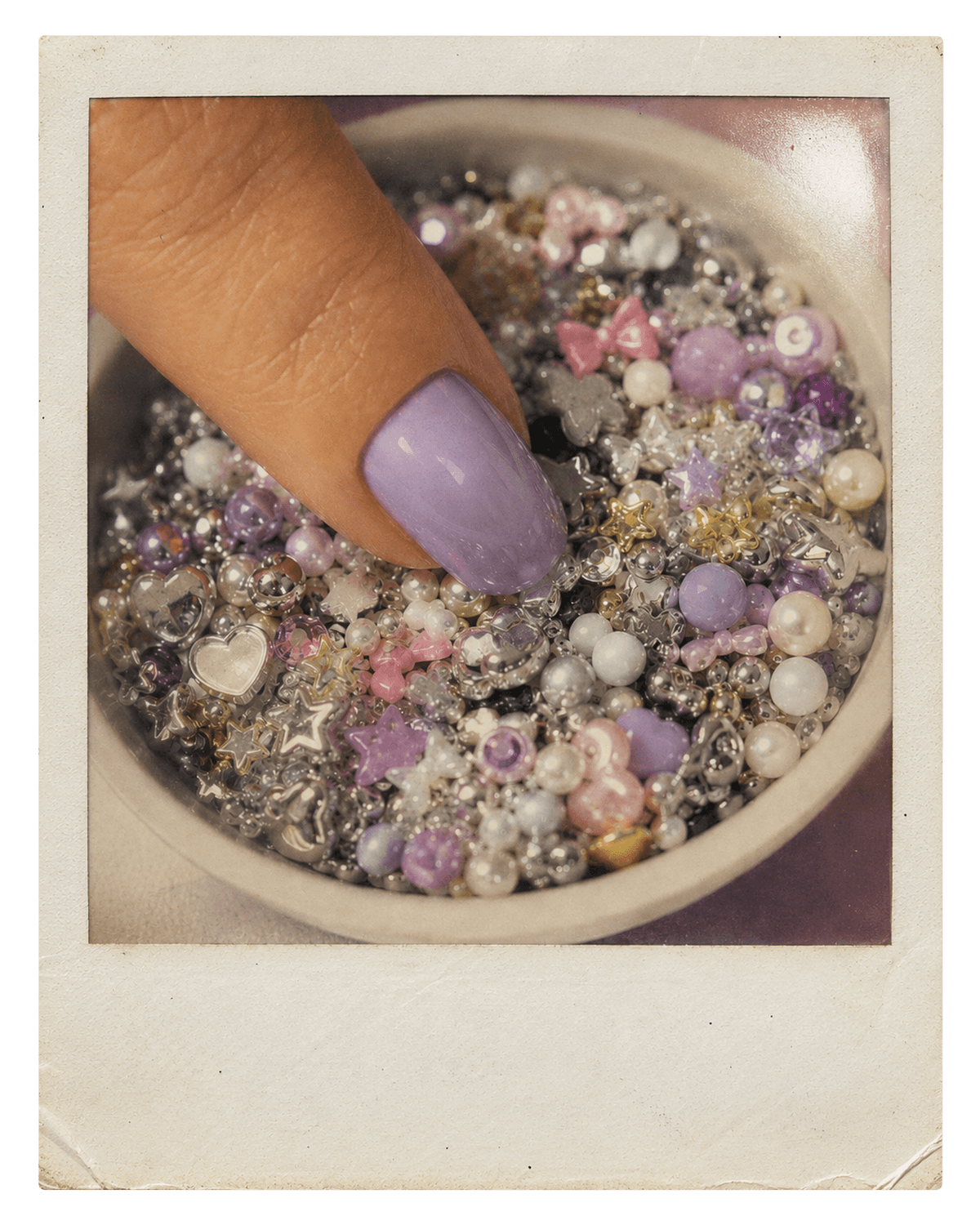 Vintage instant photo of a lavender chrome nail beside sparkling charms.