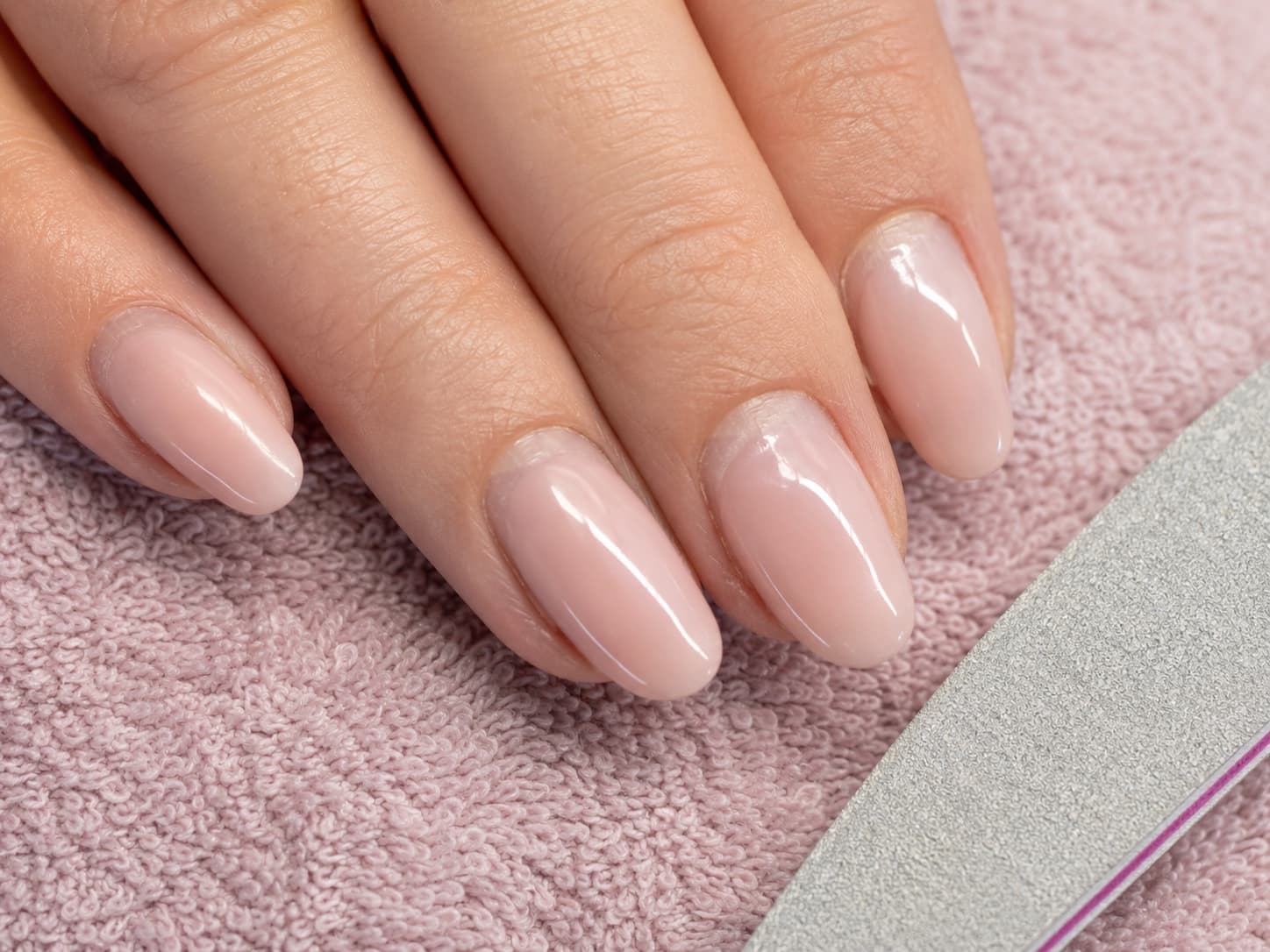 Almond nude shimmer manicure on a hand resting on a dusty pink towel beside a zebra-print nail file.