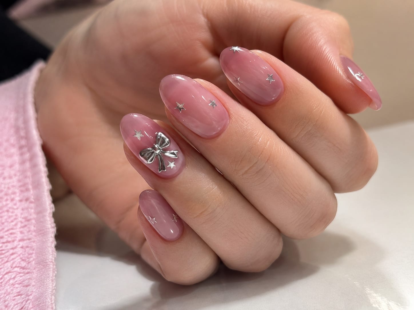 Almond pink jelly nails with silver bow charms and tiny star accents arranged on a pink towel.