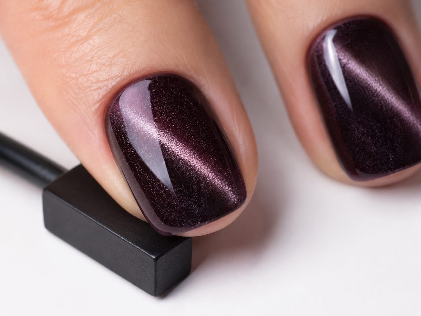 Macro of a single nail with deep burgundy plum cat-eye magnetic gel and a high-gloss finish.