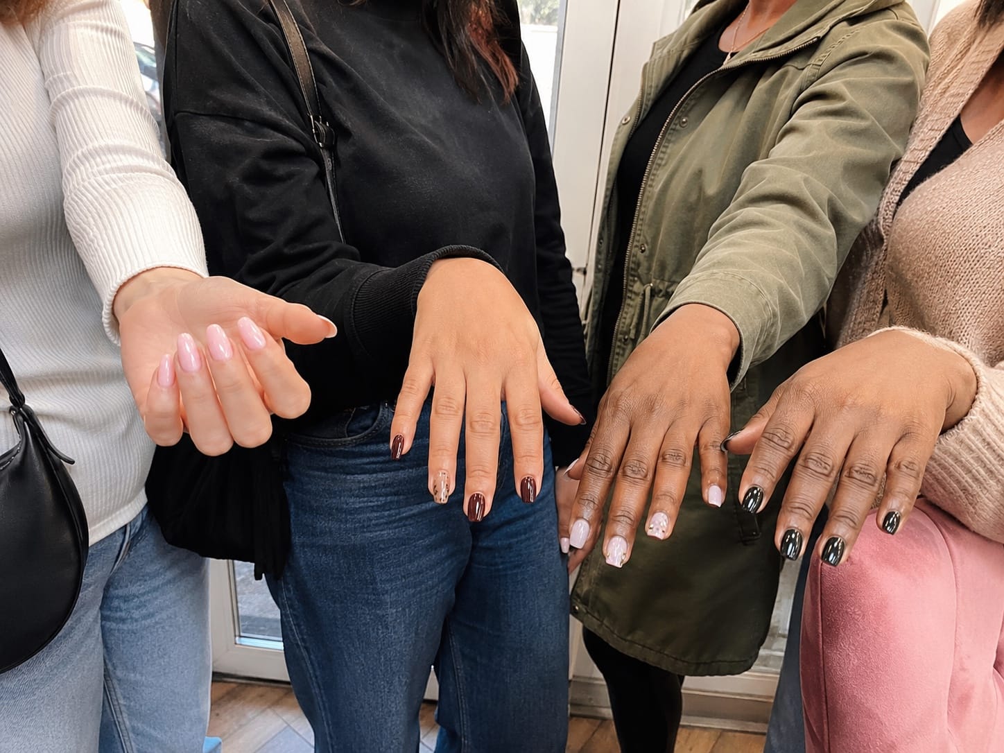 Four friends standing near a glass salon door, comparing freshly done manicures.