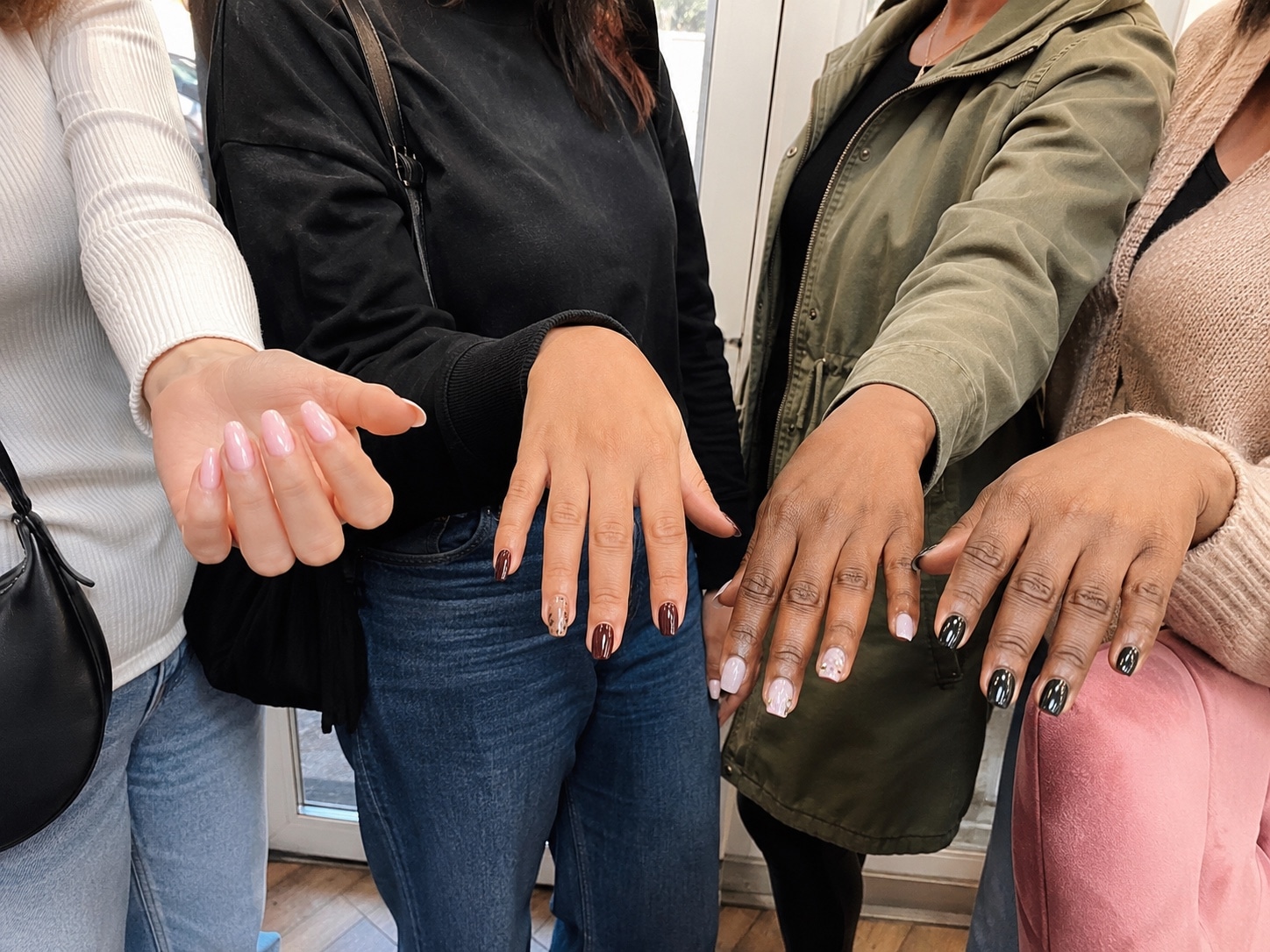 Four friends standing near a glass salon door, comparing freshly done manicures.