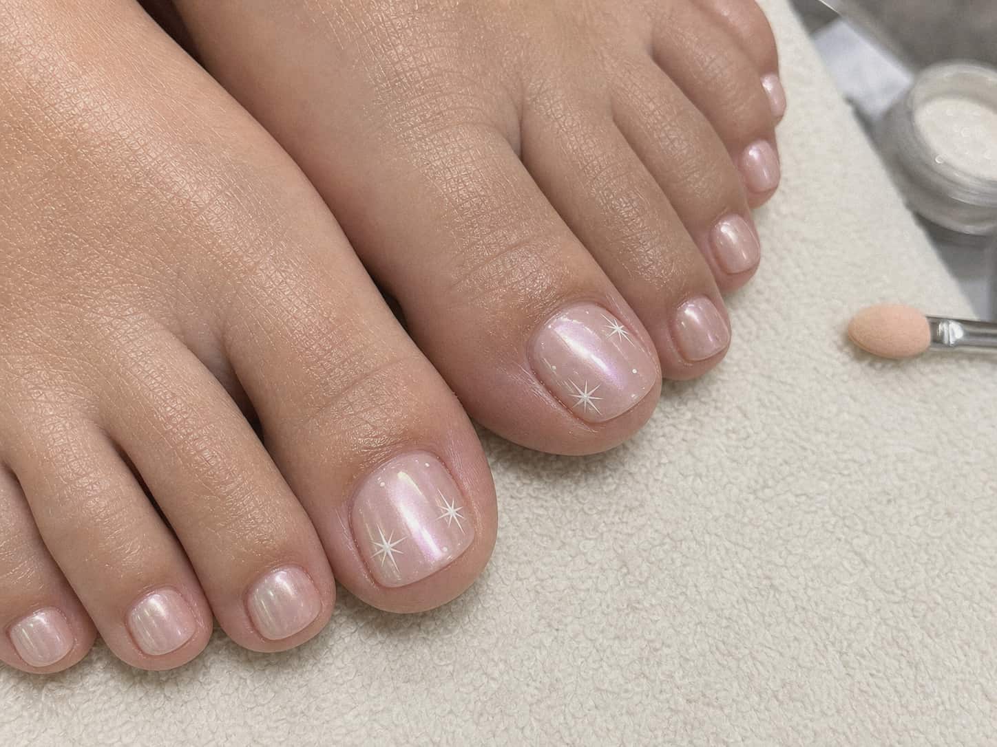 Tight close-up of a subtle pearl chrome pedicure with tiny white star accents on the big toenails.