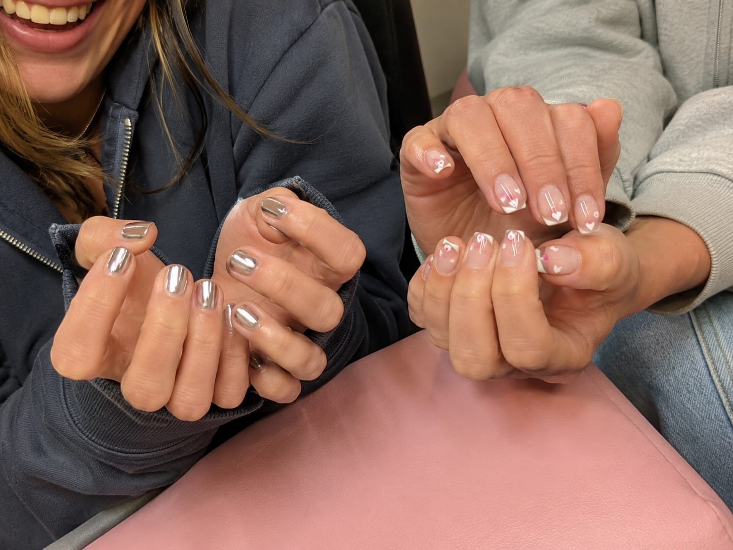 Two friends side by side comparing shiny silver chrome and clear French tip manicures.
